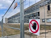 Statybinė tvora aplink angarą su draudžiamuoju ženklu